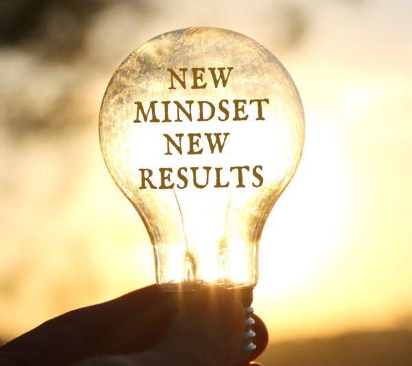 Hand holding a light bulb with the text new mindset in front of the bright sun -- signaling better ideas for a brighter tomorrow.
