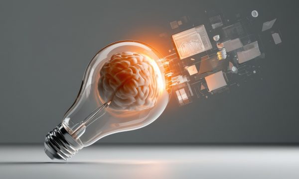 A concept image showing a transparent light bulb with a human brain inside, glowing with an orange light. the light bulb is tilted and rests on a light gray surface, against a darker gray background. various digital elements and abstract icons, including a computer screen with graphs, an envelope, stacked coins, folders, and geometric shapes, are floating and emanating from the light bulb's right side.