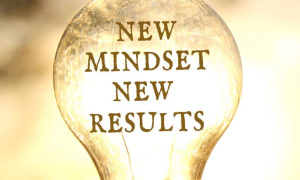 Hand holding a light bulb with the text new mindset in front of the bright sun -- signaling better ideas for a brighter tomorrow.